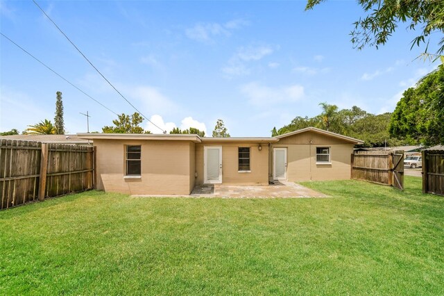 rear view of house with a fenced backyard, a patio area, concrete block siding, and a yard