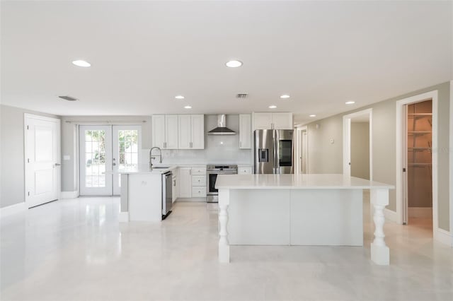 kitchen featuring backsplash, appliances with stainless steel finishes, a center island, white cabinetry, and wall chimney range hood