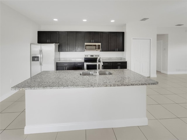 kitchen with light stone countertops, stainless steel appliances, an island with sink, and sink