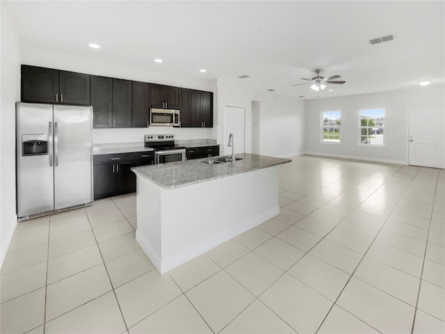 kitchen featuring appliances with stainless steel finishes, light stone counters, sink, ceiling fan, and a center island with sink