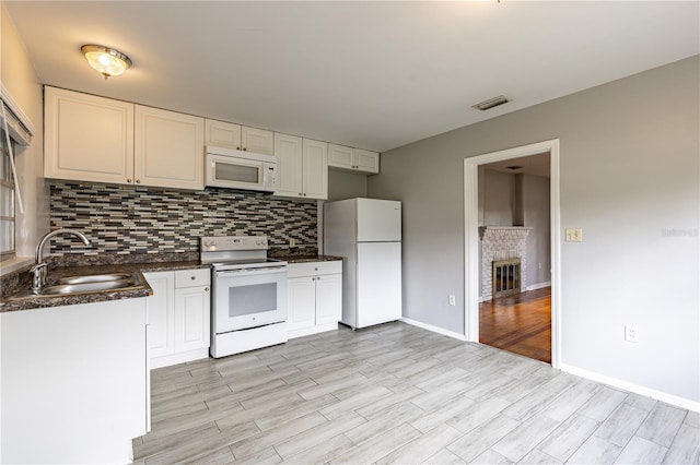 kitchen featuring light hardwood / wood-style floors, sink, white appliances, white cabinets, and a brick fireplace