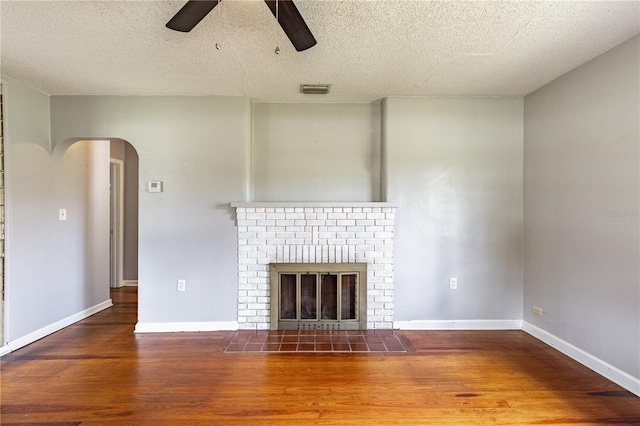 unfurnished living room with a fireplace, wood-type flooring, ceiling fan, and a textured ceiling