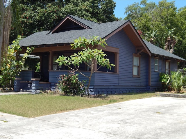 view of front of property featuring covered porch, concrete driveway, a front yard, and a shingled roof