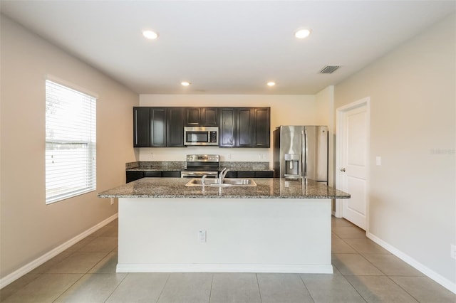 kitchen with dark stone counters, light tile patterned floors, sink, an island with sink, and appliances with stainless steel finishes