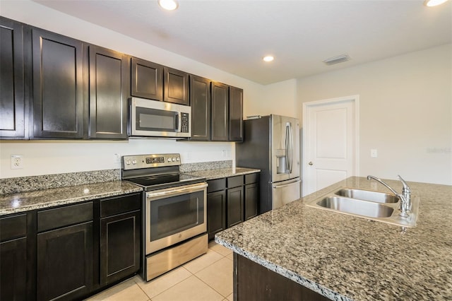 kitchen with appliances with stainless steel finishes, light tile patterned flooring, sink, and light stone countertops