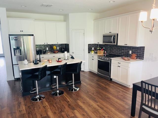 kitchen featuring appliances with stainless steel finishes, white cabinetry, hanging light fixtures, a kitchen island with sink, and dark hardwood / wood-style flooring