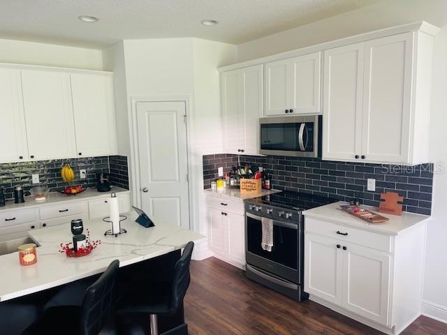 kitchen with tasteful backsplash, appliances with stainless steel finishes, dark hardwood / wood-style flooring, and white cabinets