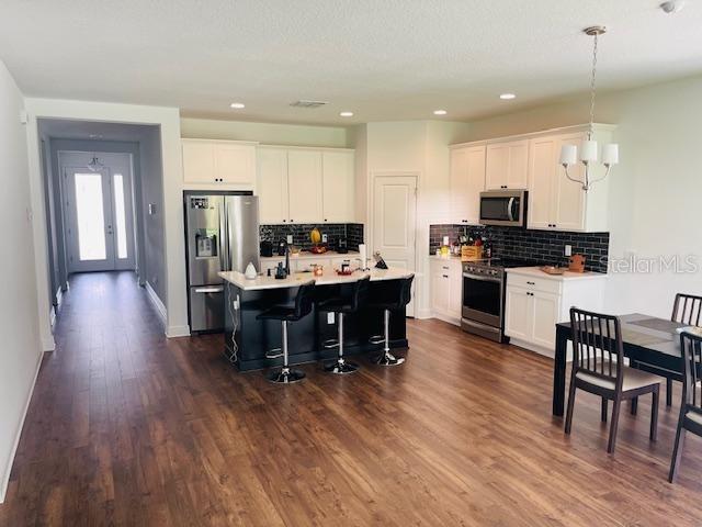 kitchen with hanging light fixtures, appliances with stainless steel finishes, a center island with sink, and white cabinets