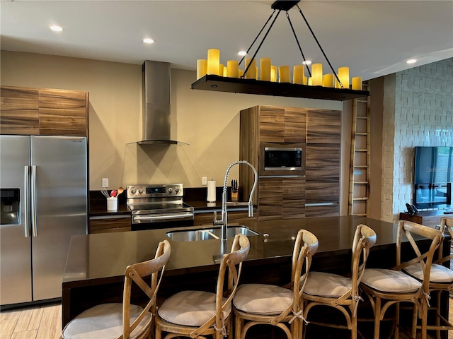 kitchen featuring stainless steel appliances, light hardwood / wood-style floors, a chandelier, sink, and wall chimney range hood