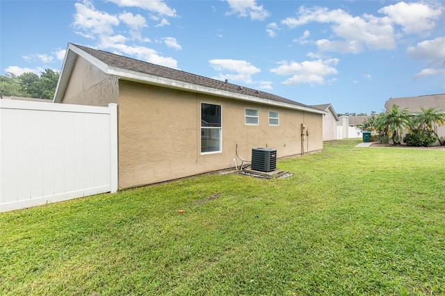 rear view of property featuring central air condition unit, fence, a lawn, and stucco siding