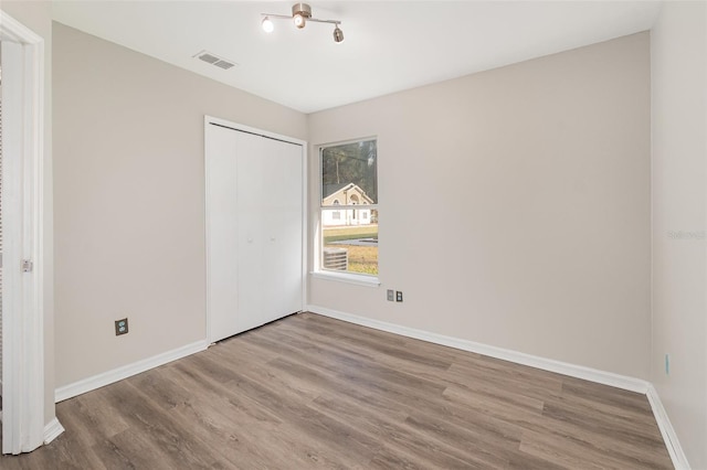 unfurnished bedroom featuring a closet, wood finished floors, visible vents, and baseboards