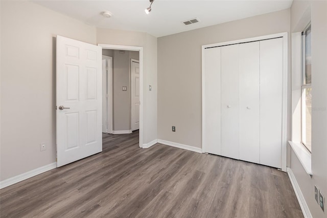 unfurnished bedroom with a closet, wood finished floors, visible vents, and baseboards