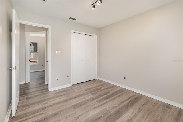 unfurnished bedroom featuring light wood-style flooring, visible vents, baseboards, a closet, and rail lighting