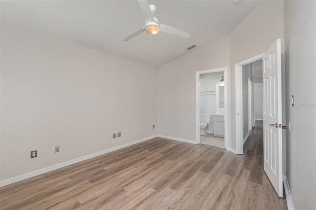 unfurnished bedroom with visible vents, light wood-style flooring, vaulted ceiling, ensuite bath, and baseboards