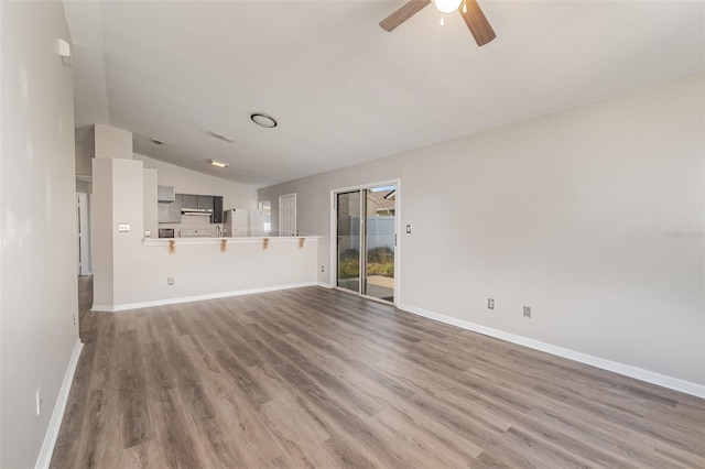 unfurnished living room with vaulted ceiling, ceiling fan, wood finished floors, and baseboards