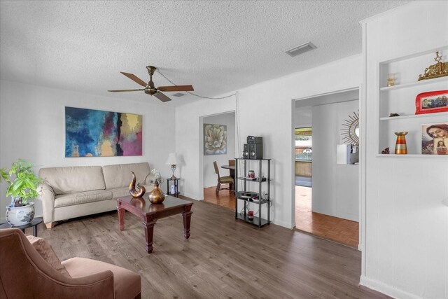 living room featuring a textured ceiling, ceiling fan, built in shelves, and dark hardwood / wood-style flooring