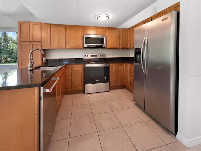 kitchen with dark stone countertops, stainless steel appliances, light tile patterned flooring, and sink