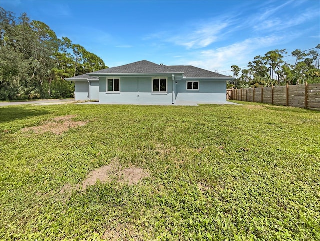 rear view of house featuring fence, a lawn, and stucco siding