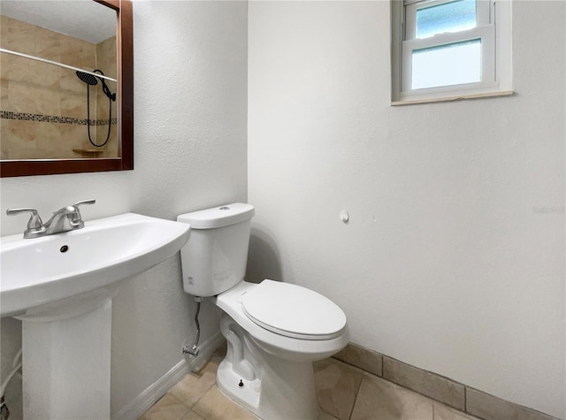 bathroom with toilet, tiled shower, sink, and tile patterned flooring