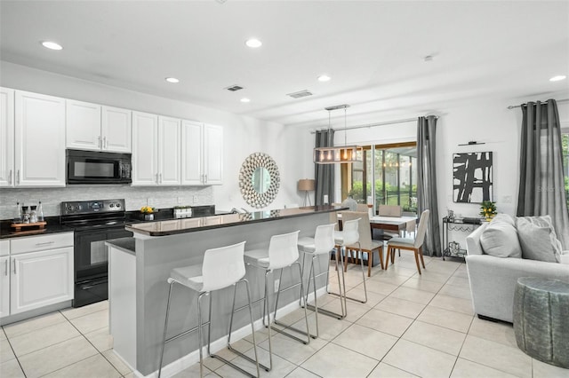kitchen featuring dark countertops, white cabinetry, open floor plan, a kitchen bar, and black appliances
