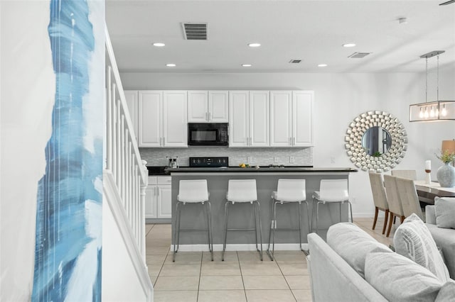 kitchen with white cabinets, hanging light fixtures, light tile patterned floors, black appliances, and a breakfast bar area