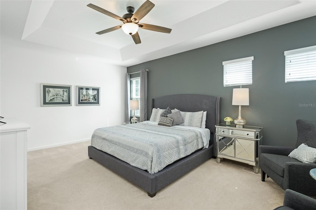 bedroom with a raised ceiling, a ceiling fan, and light colored carpet
