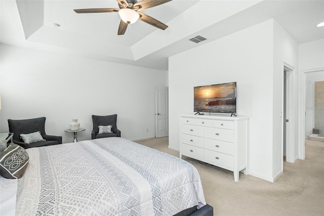 carpeted bedroom with a raised ceiling, connected bathroom, and ceiling fan