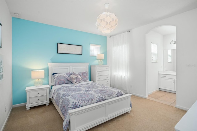 bedroom featuring arched walkways, multiple windows, baseboards, and light colored carpet