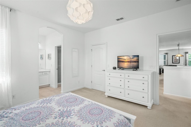 bedroom with arched walkways, light colored carpet, connected bathroom, and visible vents