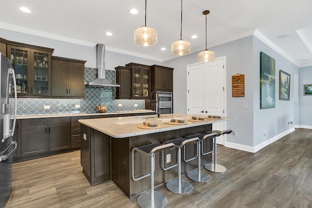 10472 Petrillo Way, Winter Garden, FL 34787 - kitchen featuring an island with sink, backsplash, wood finished floors, wall chimney exhaust hood, and light stone countertops