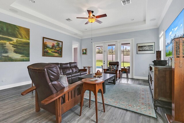 living room featuring dark hardwood / wood-style flooring, ceiling fan, a raised ceiling, and ornamental molding