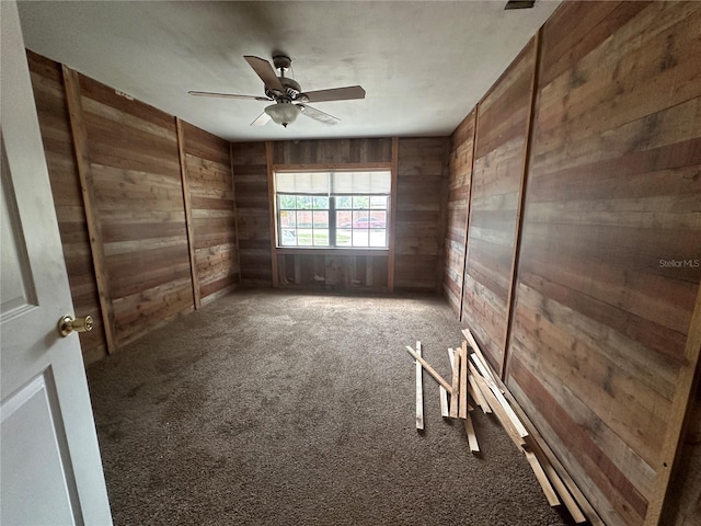 carpeted spare room with ceiling fan and wood walls