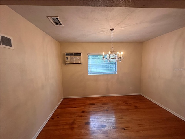 spare room with a wall unit AC, hardwood / wood-style flooring, and a notable chandelier