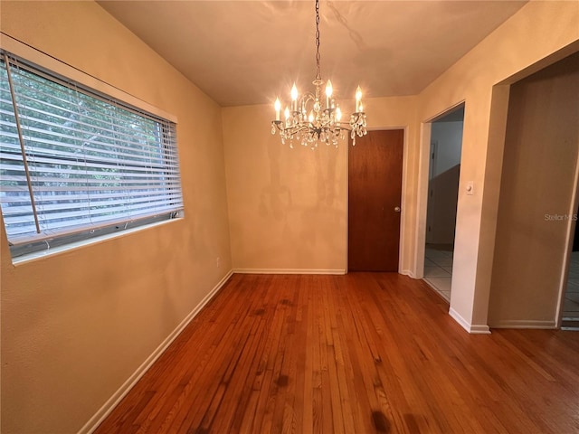 unfurnished dining area with hardwood / wood-style floors and an inviting chandelier