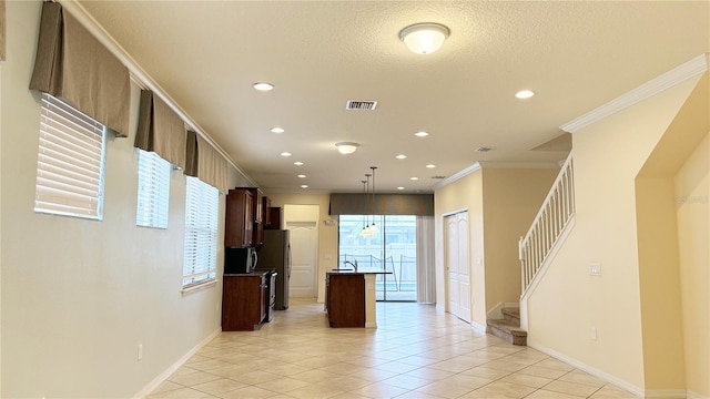 kitchen featuring a center island with sink, light tile patterned floors, crown molding, stainless steel fridge, and pendant lighting