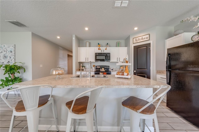 kitchen featuring a breakfast bar area, black appliances, sink, white cabinetry, and a large island with sink