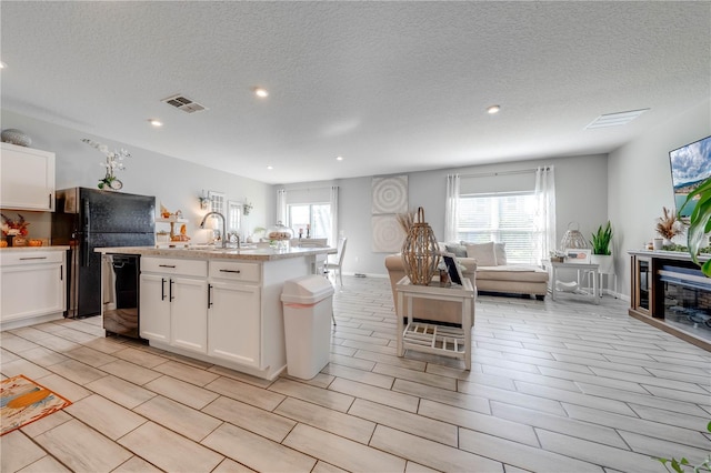 kitchen with black appliances, sink, an island with sink, light stone countertops, and light hardwood / wood-style floors