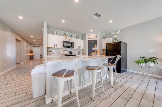 kitchen featuring a textured ceiling, light stone countertops, black appliances, light hardwood / wood-style flooring, and white cabinetry