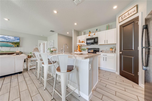 kitchen featuring black appliances, a breakfast bar area, white cabinetry, and a kitchen island with sink