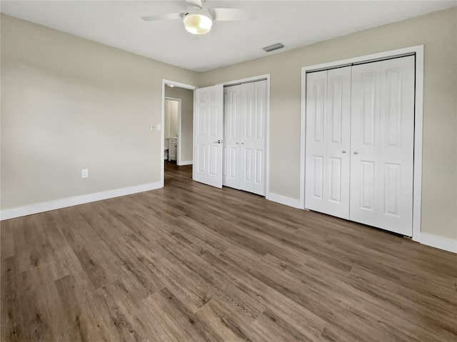 unfurnished bedroom with dark wood-type flooring, ceiling fan, and two closets