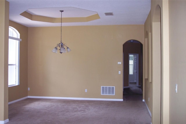 carpeted spare room featuring arched walkways, a tray ceiling, visible vents, and baseboards