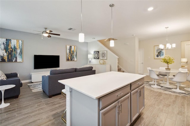 kitchen featuring hanging light fixtures, ceiling fan with notable chandelier, a kitchen island, light wood-type flooring, and a kitchen bar