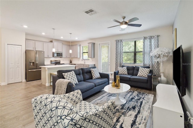 living room featuring light wood-type flooring, ceiling fan, and sink