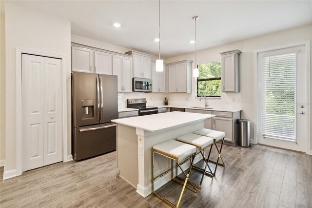 kitchen with gray cabinets, a center island, sink, appliances with stainless steel finishes, and decorative light fixtures