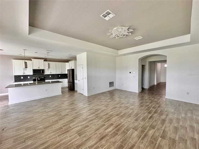 unfurnished living room with light wood-type flooring, a raised ceiling, and sink