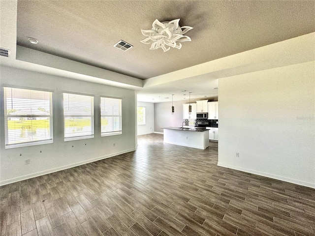 unfurnished living room featuring a raised ceiling, dark hardwood / wood-style flooring, and sink