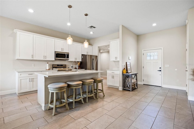 kitchen featuring pendant lighting, a breakfast bar, white cabinets, an island with sink, and appliances with stainless steel finishes