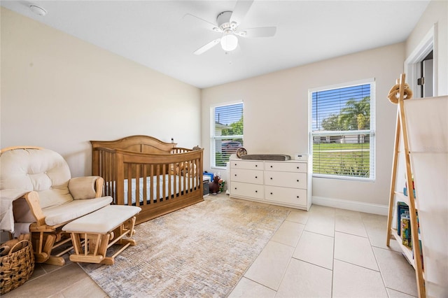 bedroom featuring ceiling fan, light tile patterned floors, and a nursery area