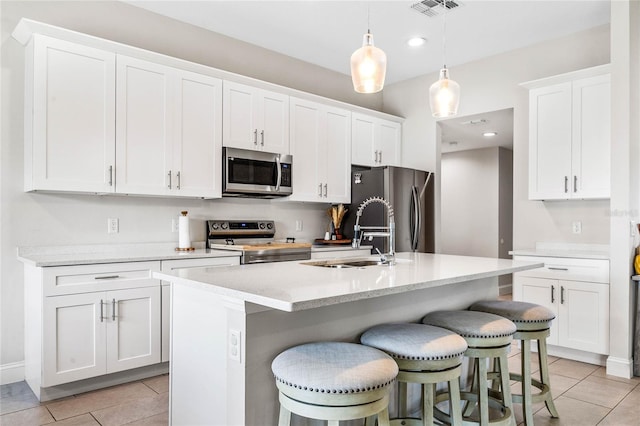 kitchen featuring appliances with stainless steel finishes, sink, decorative light fixtures, white cabinets, and an island with sink