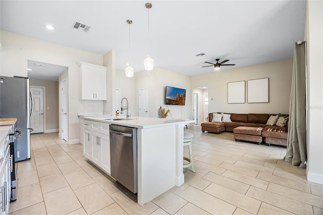 kitchen featuring white cabinets, stainless steel appliances, hanging light fixtures, and an island with sink